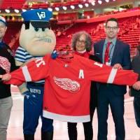 Alumni pose with Louie the Laker while holding up a Red Wings Jersey at the Detroit Red Wings GVSU Night